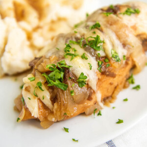 Crockpot French Onion Chicken on a white plate with mashed potatoes and parsley on top.
