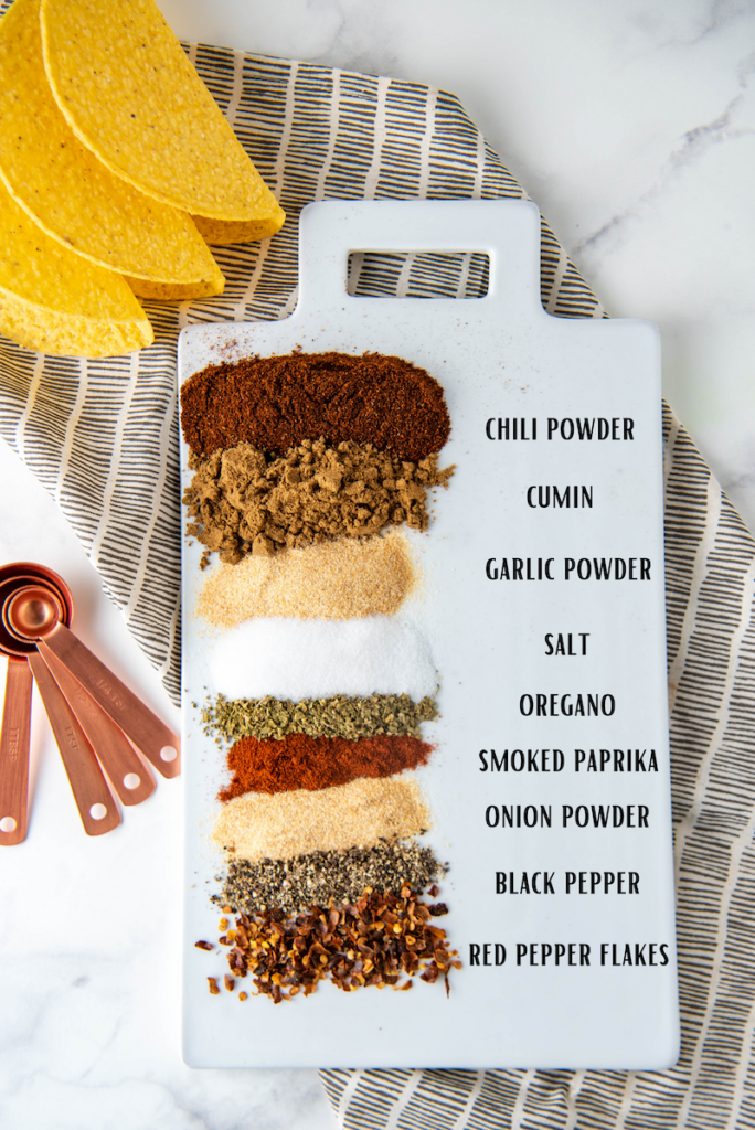 Seasonings lined up on a platter on top of a tea towel with taco shells.