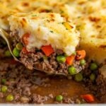 A portion of shepherd's pie is being lifted from a casserole dish.