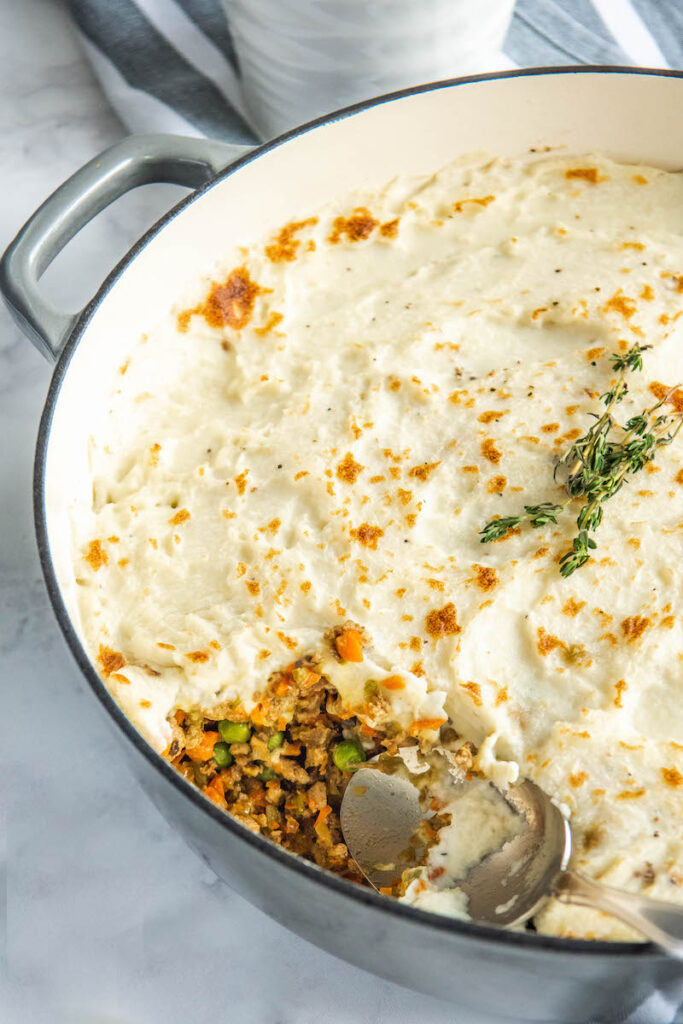 Shepherd’s Pie in a large pan with a spoon taking a scoop out of it.