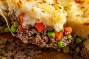 A portion of shepherd's pie is being lifted from a casserole dish.