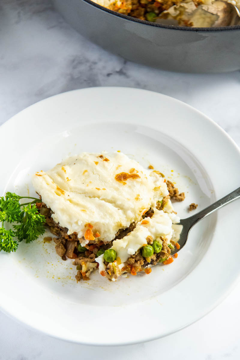Shepherd’s pie on a white plate with a fork and parsley.