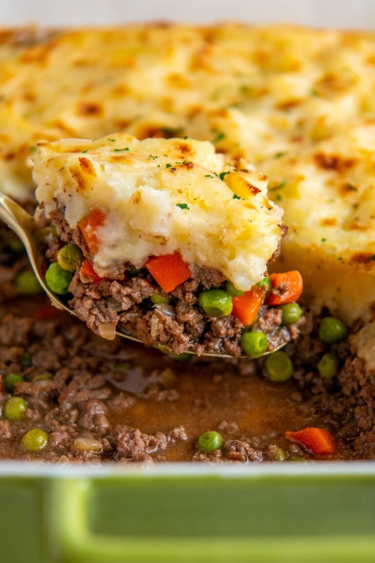 A portion of shepherd's pie is being lifted from a casserole dish.