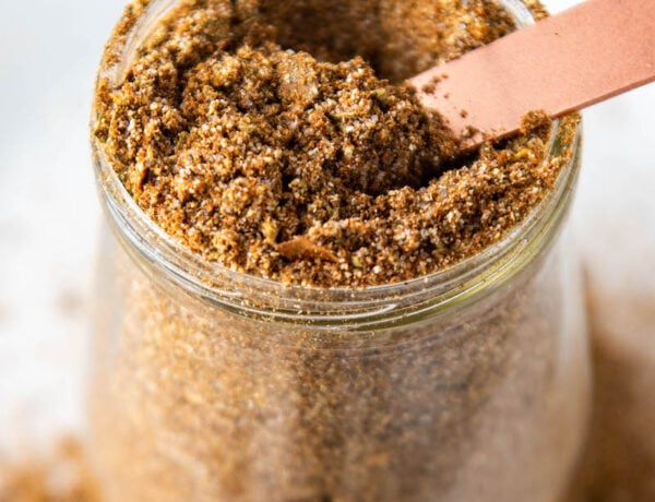 Up close image of taco seasoning in a glass jar with a measuring spoon.