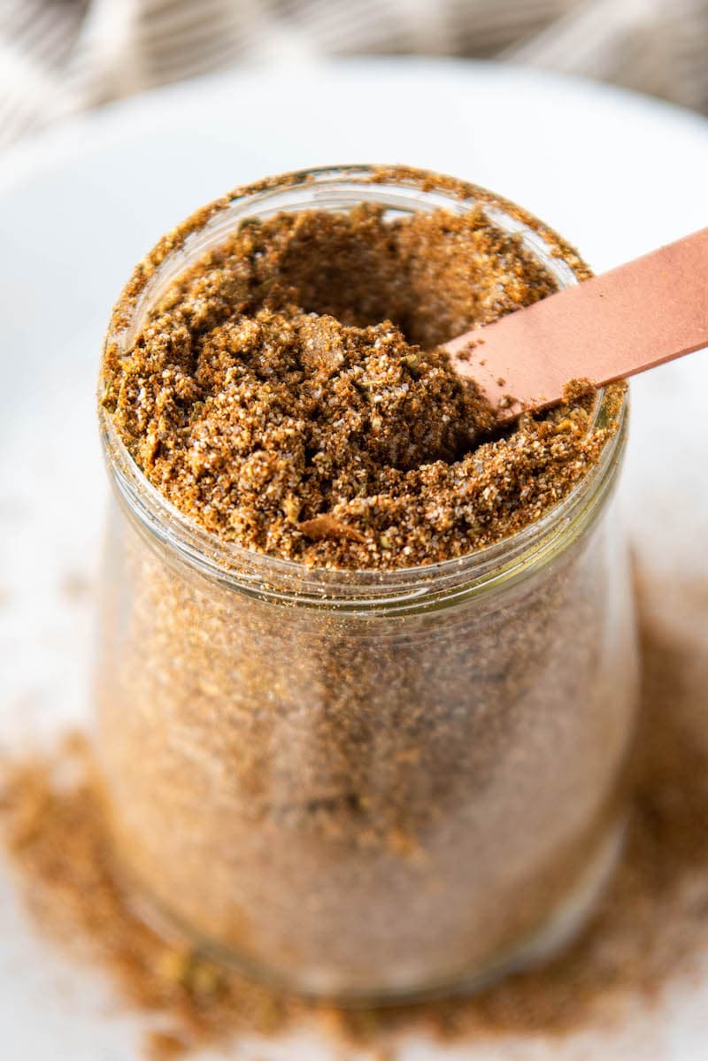 Up close image of taco seasoning in a glass jar with a measuring spoon.