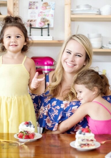 Mom and two daughters at a table with cake on a cake stand.