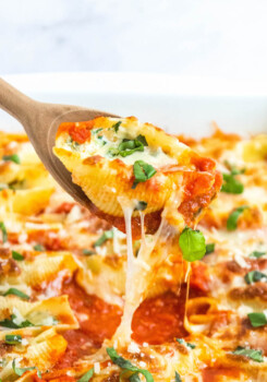 Stuffed shells with spinach being pulled out of casserole dish with wooden spoon.