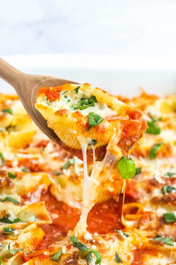 Stuffed shells with spinach being pulled out of casserole dish with wooden spoon.