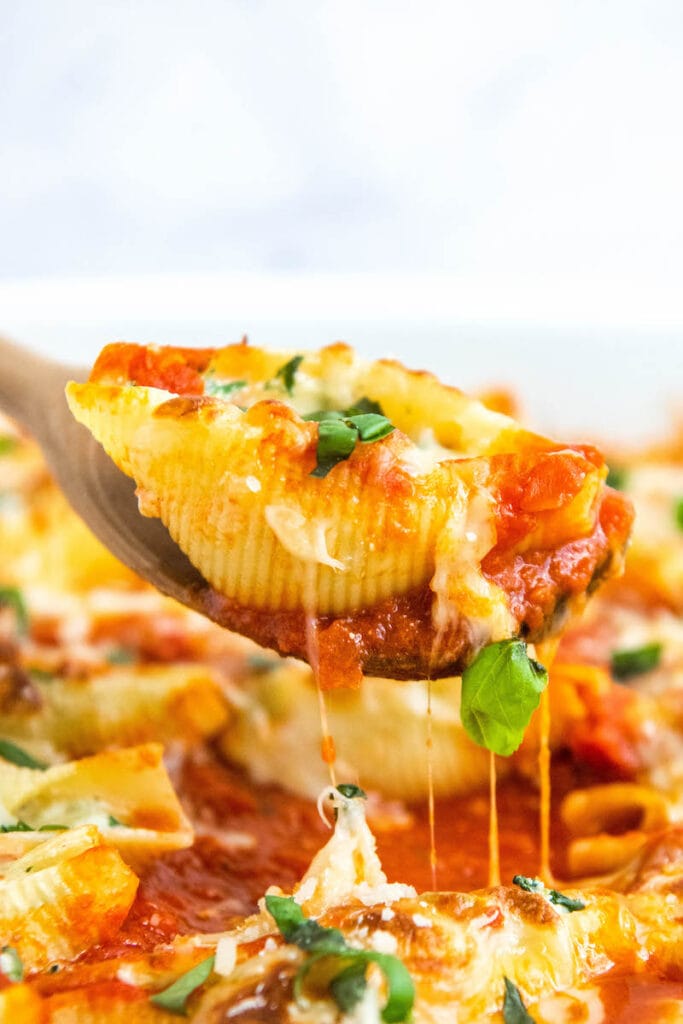 Close up shot of shells with cheese on a wooden spoon.