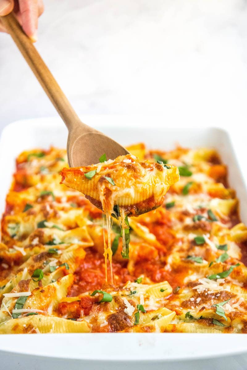 pan filled with stuffed shells with a shell being pulled out by a wooden spoon.