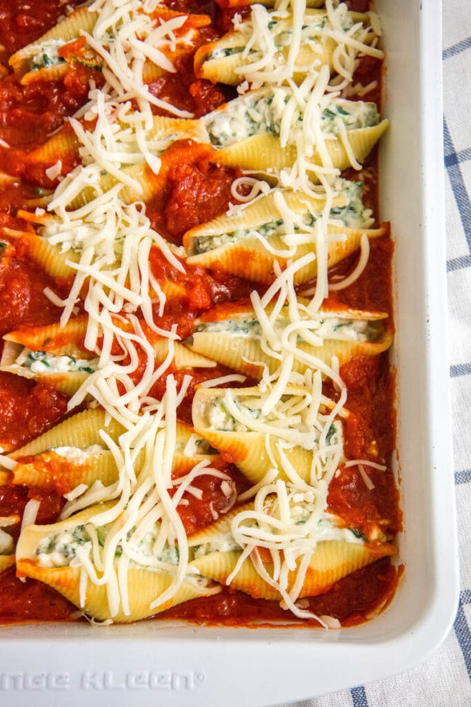 Unbaked stuffed shells in casserole dish with marinara and cheese on top.