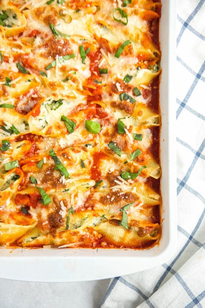 Stuffed shells with spinach in a casserole dish with basil on top.