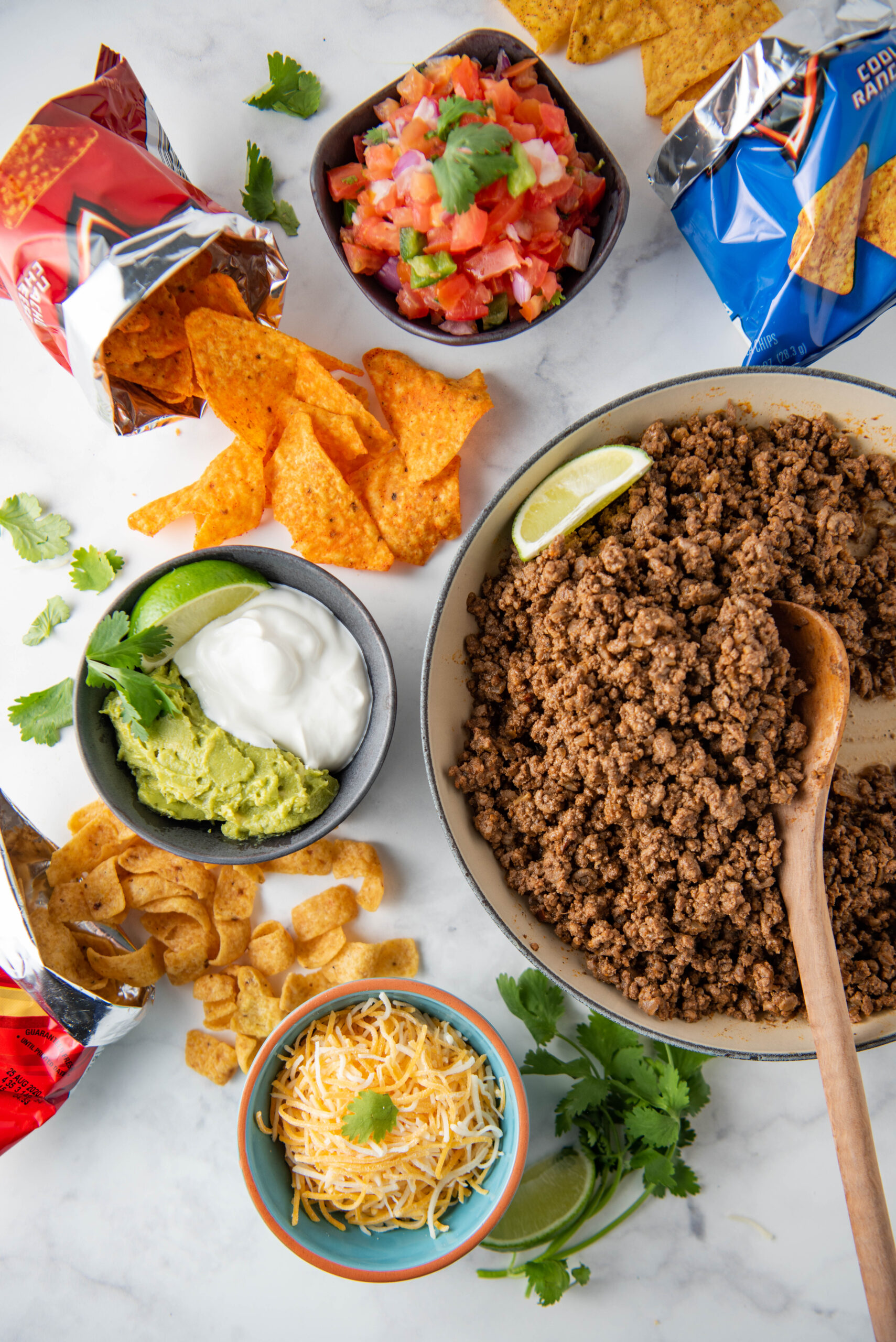 All ingredients for walking tacos are spread out on a white table