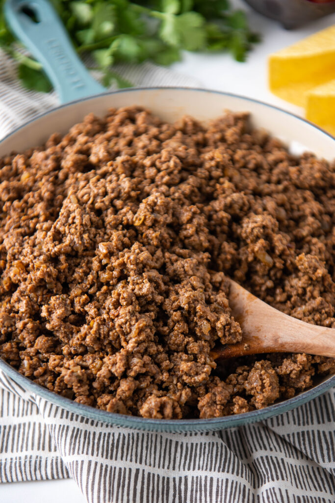 A pot of ground beef is being stirred with a wooden spoon