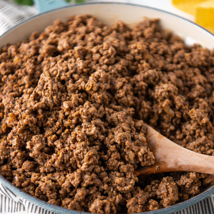 A pot of ground beef is being stirred with a wooden spoon