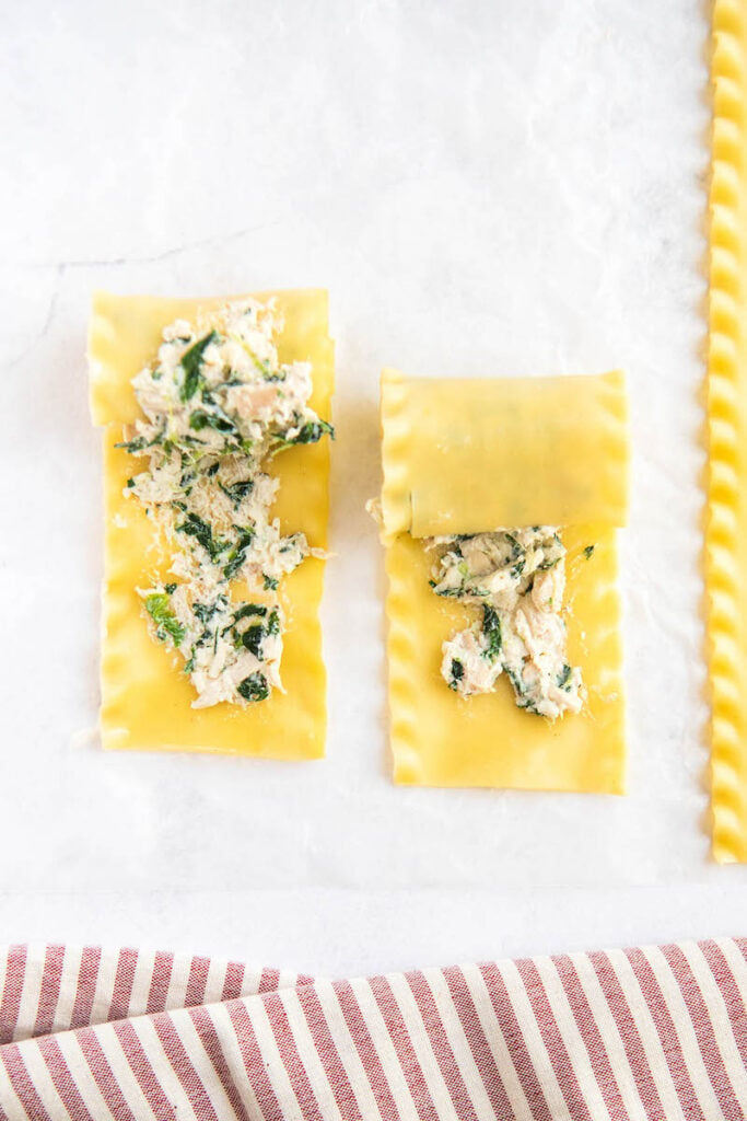 Lasagna noodles are being rolled up on a white surface