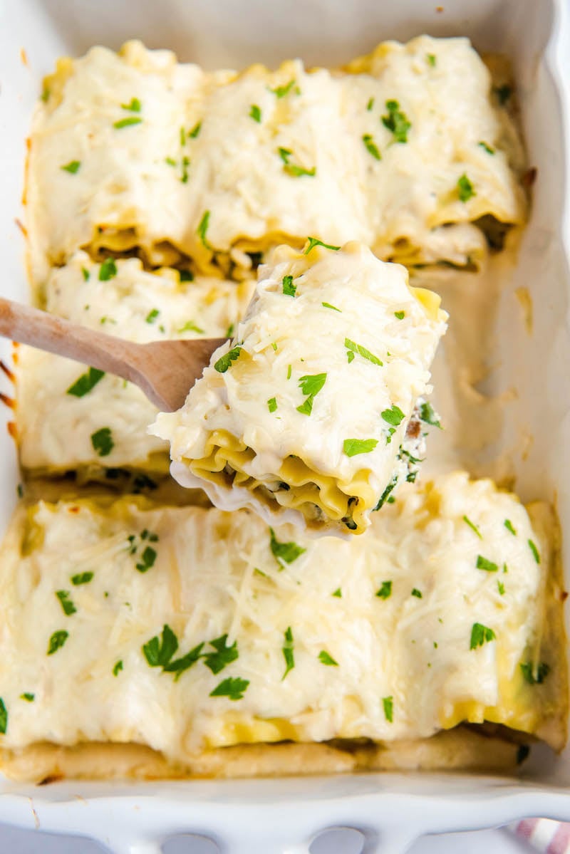 Completed white chicken lasagna rollups are being scooped out of a casserole dish