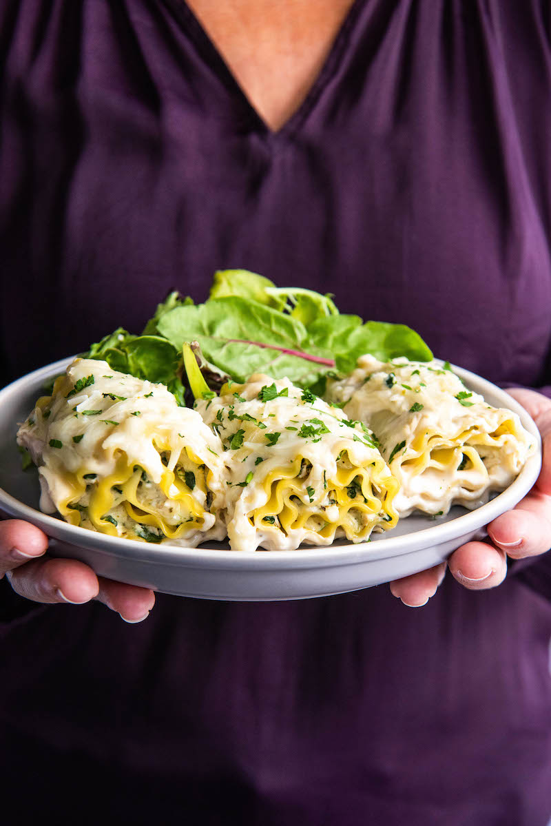 A plate of white chicken lasagna rollups is being held by a woman in a purple shirt