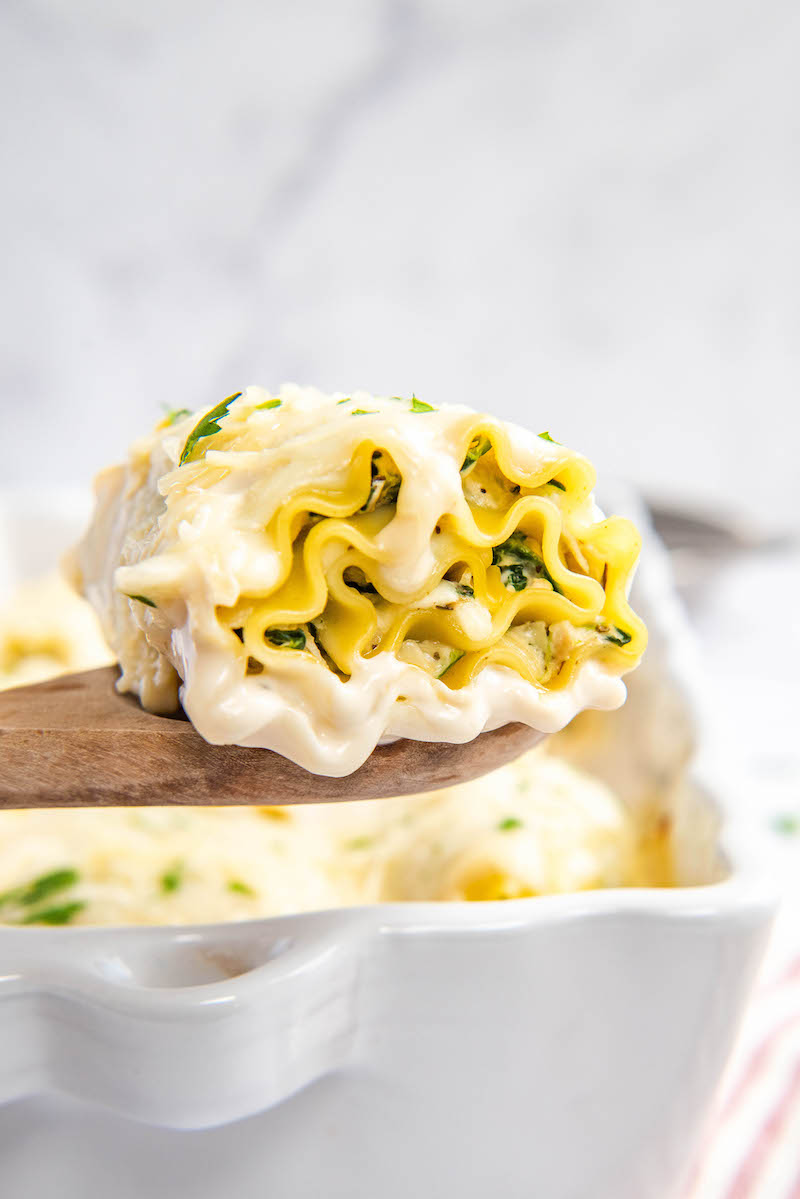 A white chicken lasagna rollup is held on a wooden spoon