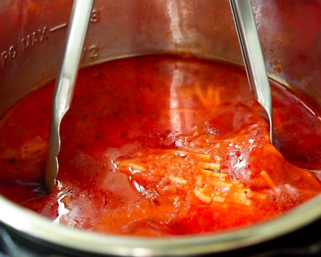 Tongs are mixing ingredients in the pressure cooker.