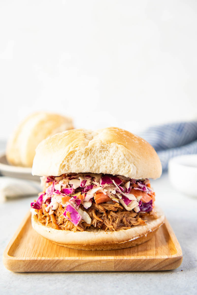 A pulled pork sandwich sits on a wooden plate