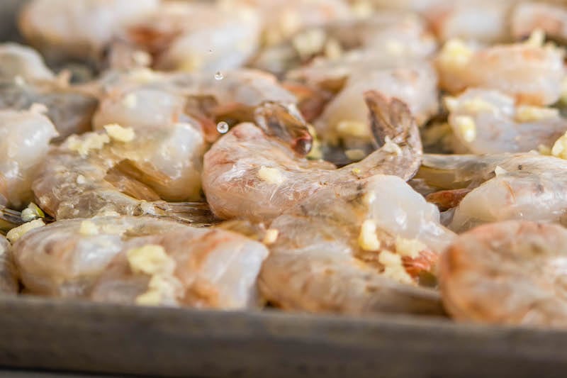 Raw shrimp arranged in an even layer on a sheet pan with garlic.