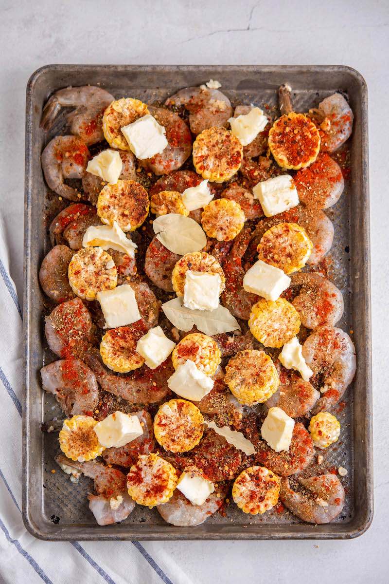 Sheet pan filled with seasoned raw shrimp and corn.