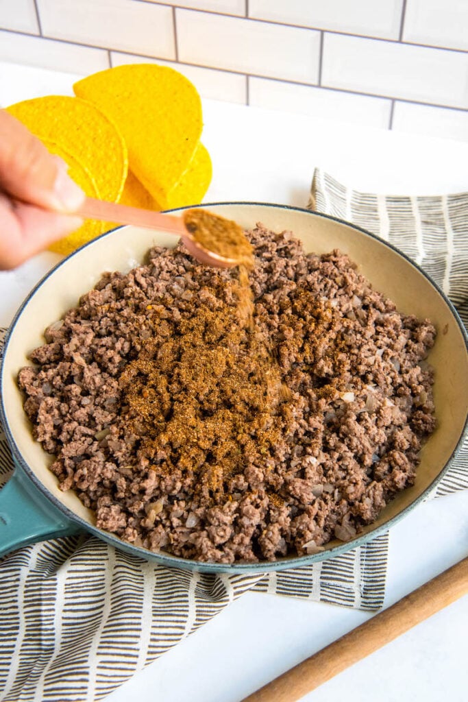 Homemade taco seasoning is being sprinkled into a skillet of ground beef