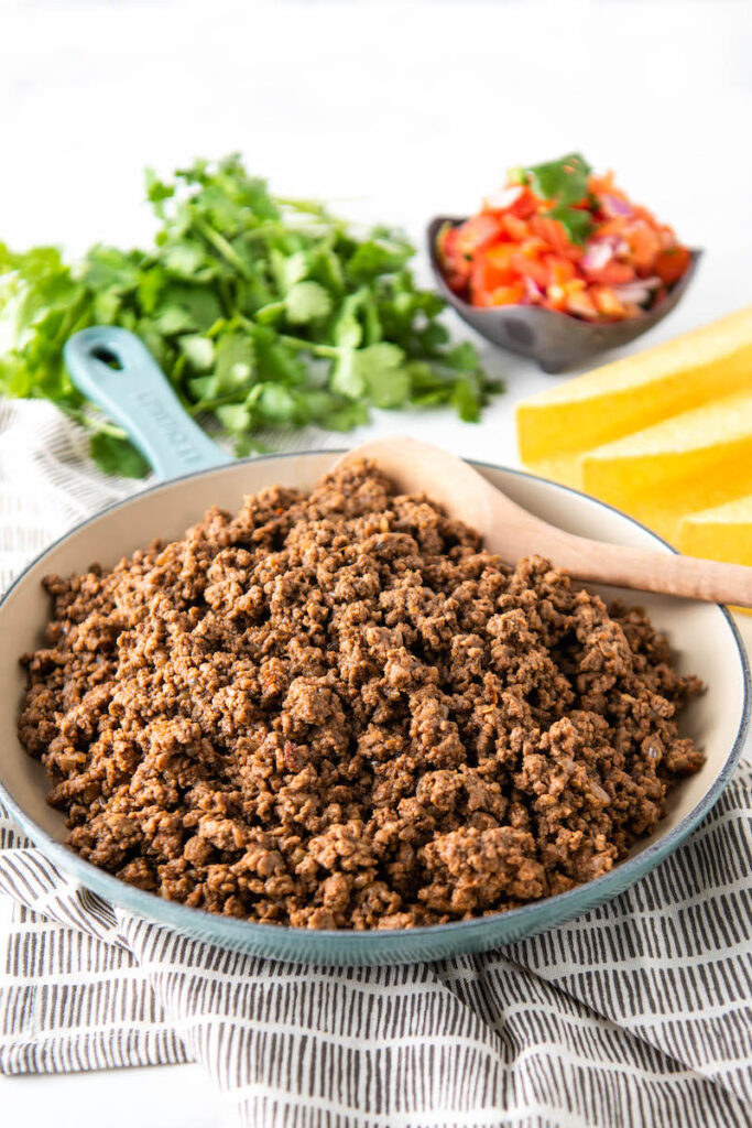 Taco meat is presented in a skillet with cilantro, pico de Gallo and taco shells around it