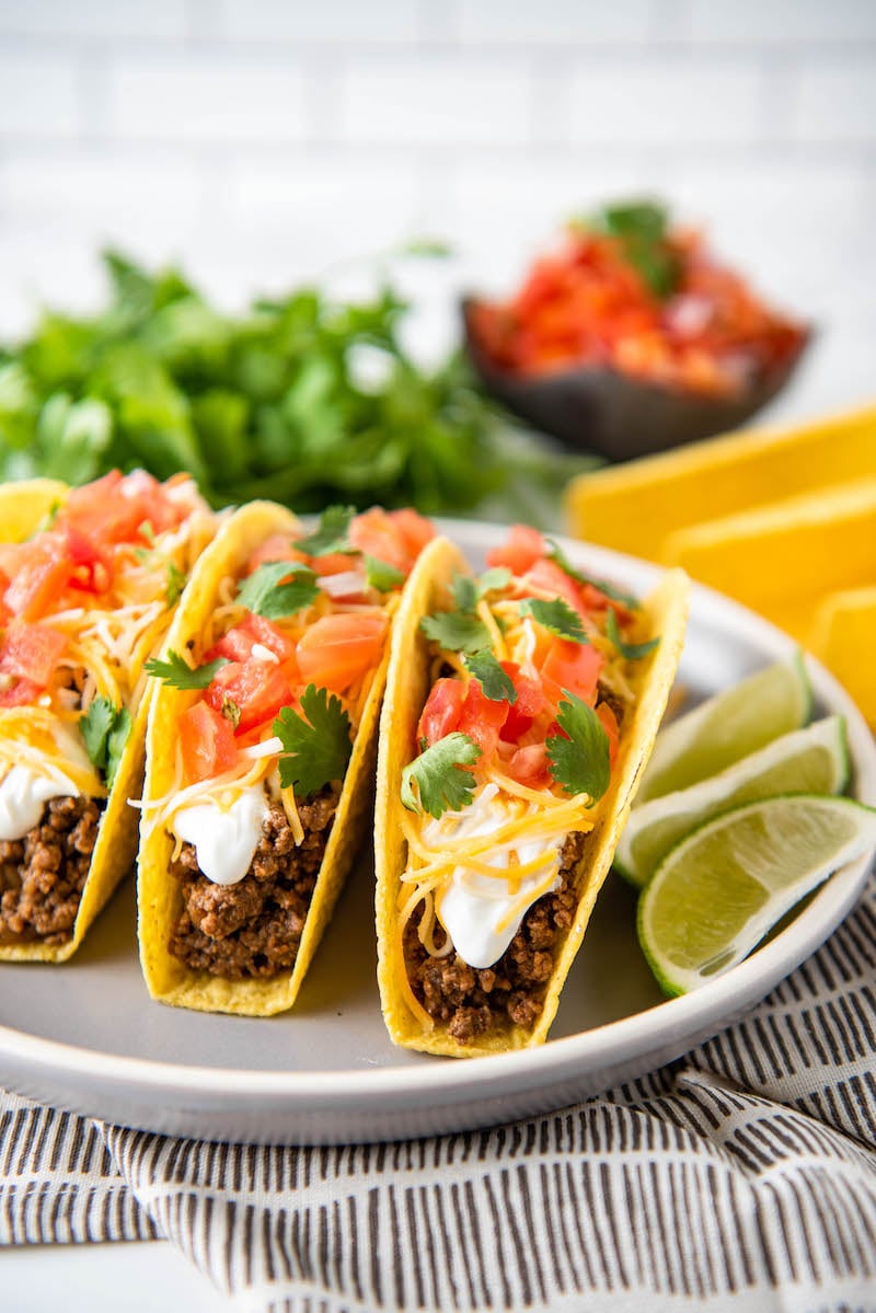 Tacos are on a white plate, placed next to a sliced lime