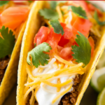 Up close image of ground taco meat in a crispy taco shell with toppings.