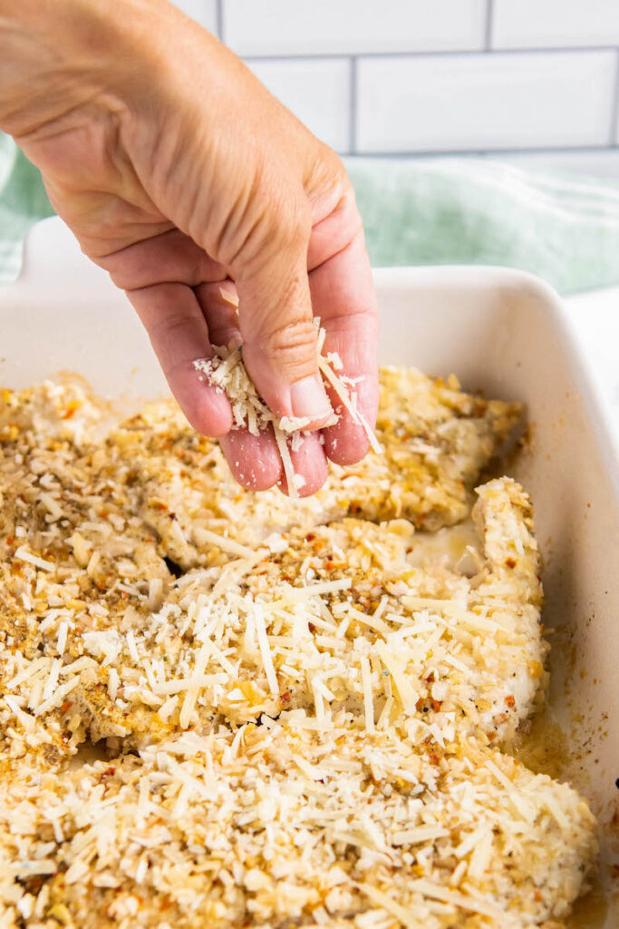 Chicken breasts being sprinkled with parmesan in a baking pan.