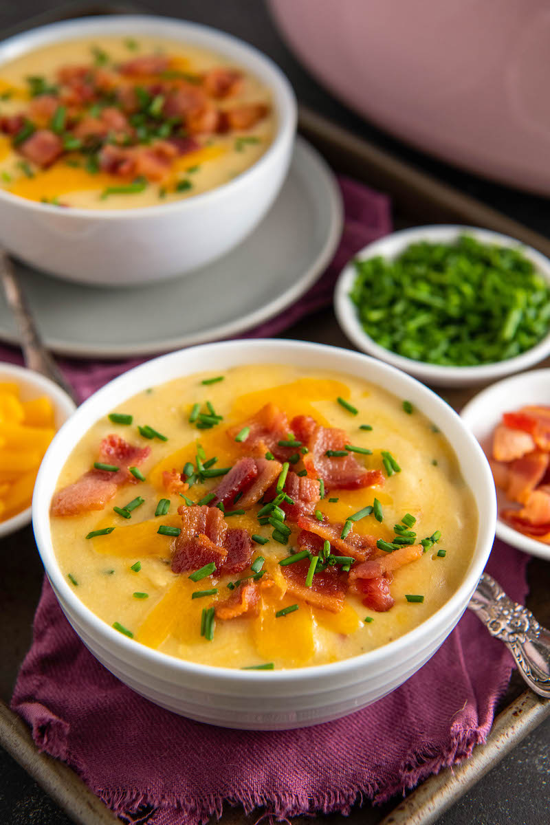 Two bowls of potato soup are on a table with a red tablecloth