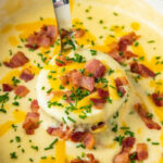 A ladle is holding a scoop of potato soup above a bowl