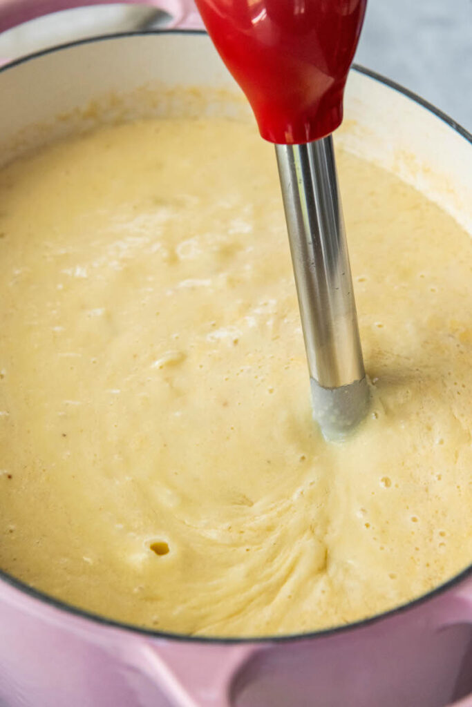 An immersion blender is blending the ingredients in the pot