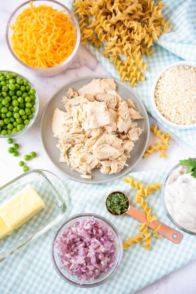 The ingredients for the tuna noodle casserole are separated on a white tabletop. 