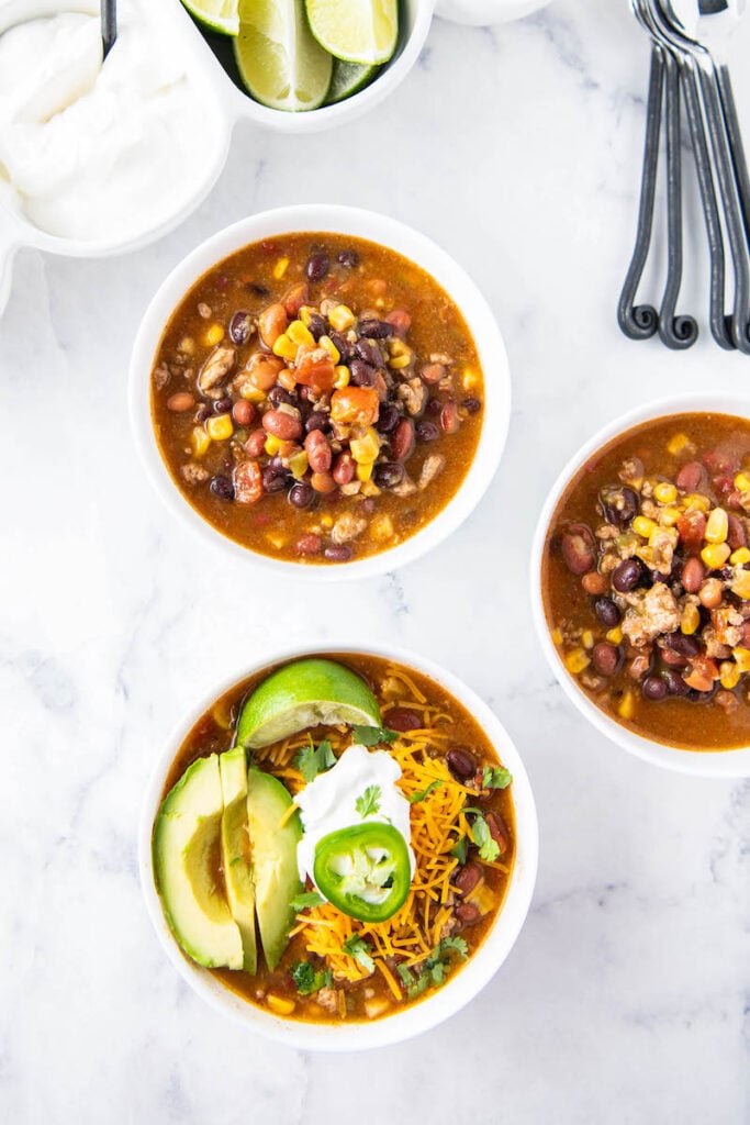 Three bowls of instant pot taco soup are on a white surface with spoons.