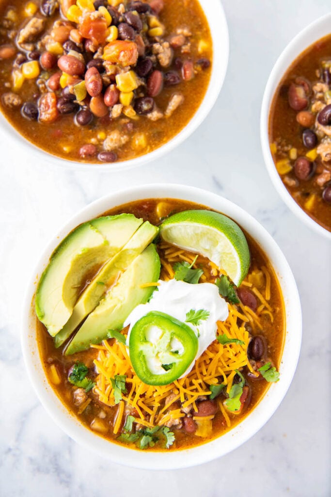 A bowl of taco soup is topped with avocado and jalapeños