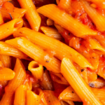Up close image of pasta in red sauce in a pan with wording on top for pinterest.