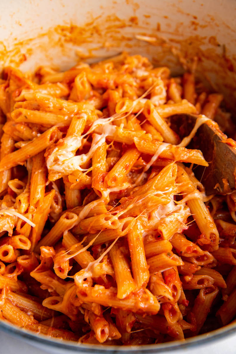 A wooden spoon is stirring the pasta and cheese, mixing them together