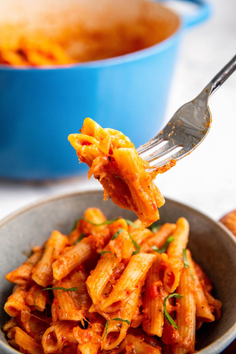 A forkful of penne noodles are lifted from a bowl