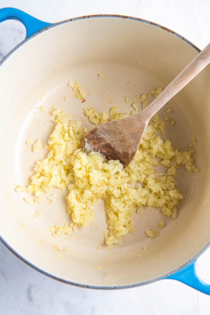 Garlic is being sautéed in a large dutch oven