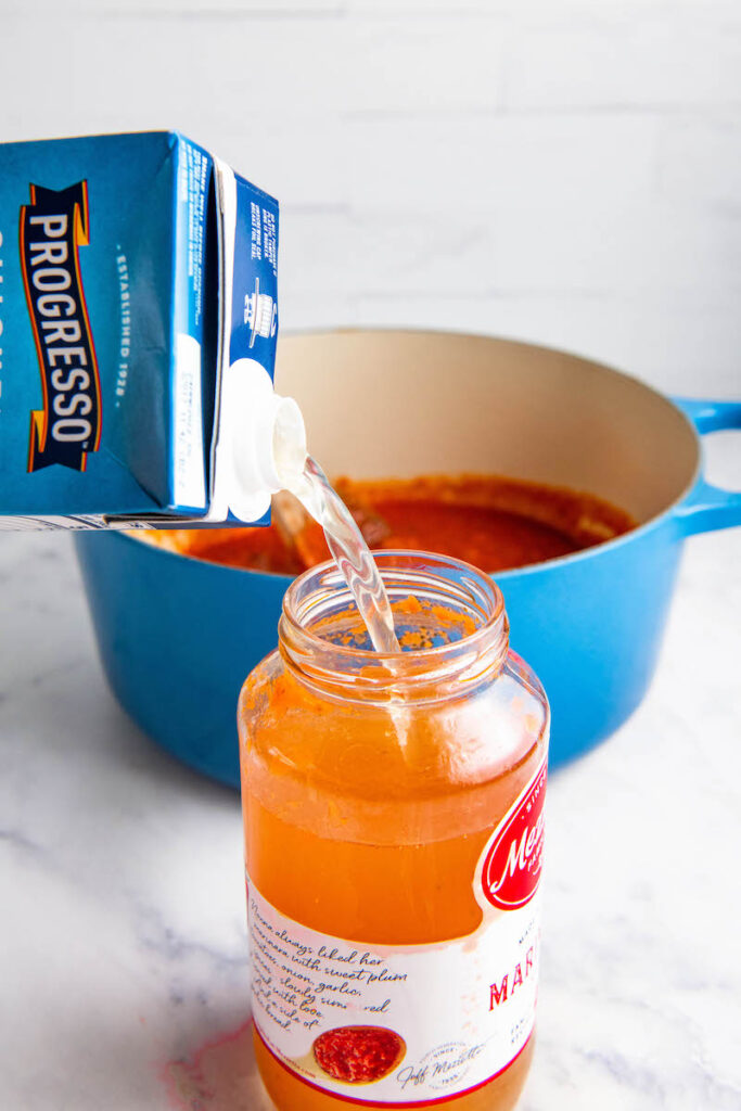 Chicken broth is poured into an empty marinara jar