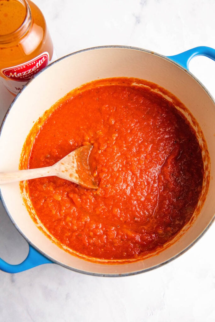 A spoon sits in a dutch oven full of red sauce