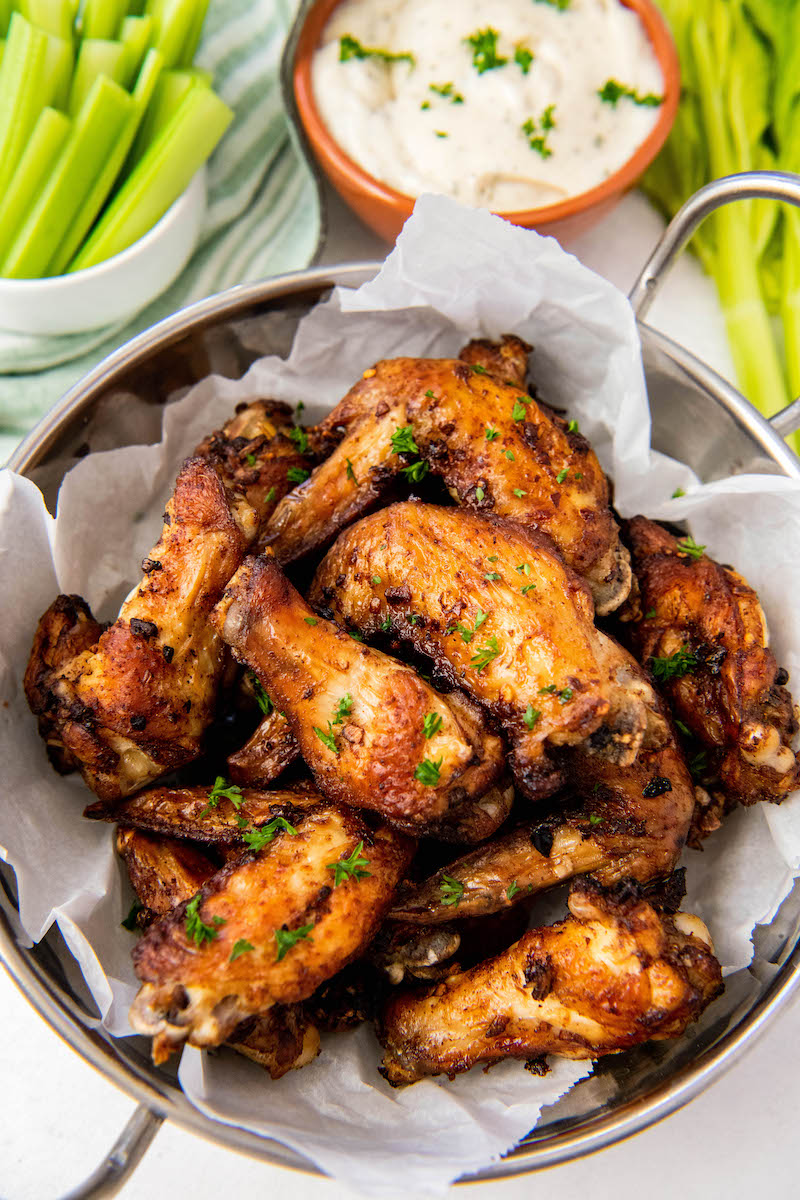 Several wings sit on a piece of parchment paper with celery and sauce in the background.