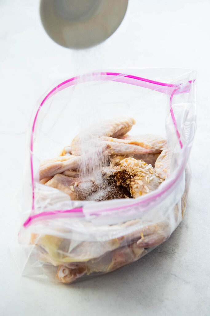 Salt is sprinkled into the plastic bag containing the uncooked chicken.
