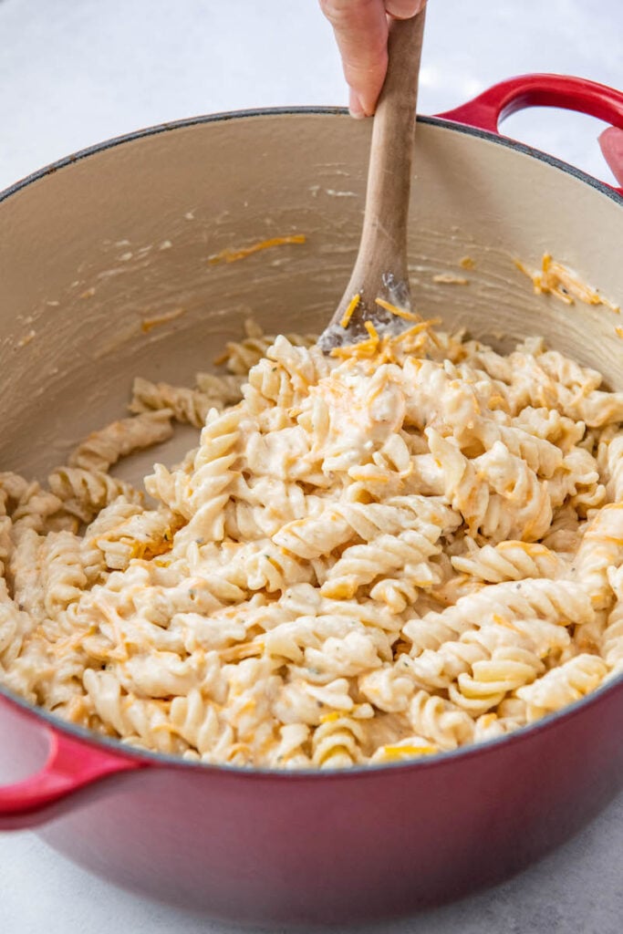 A wooden spoon is mixing the creamy pasta in a large pot.