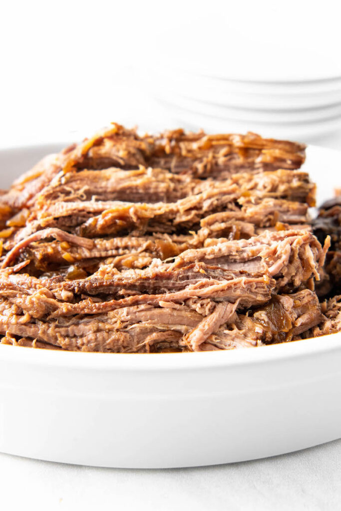 A close up shot shows shredded beef stacked in a clean white bowl.
