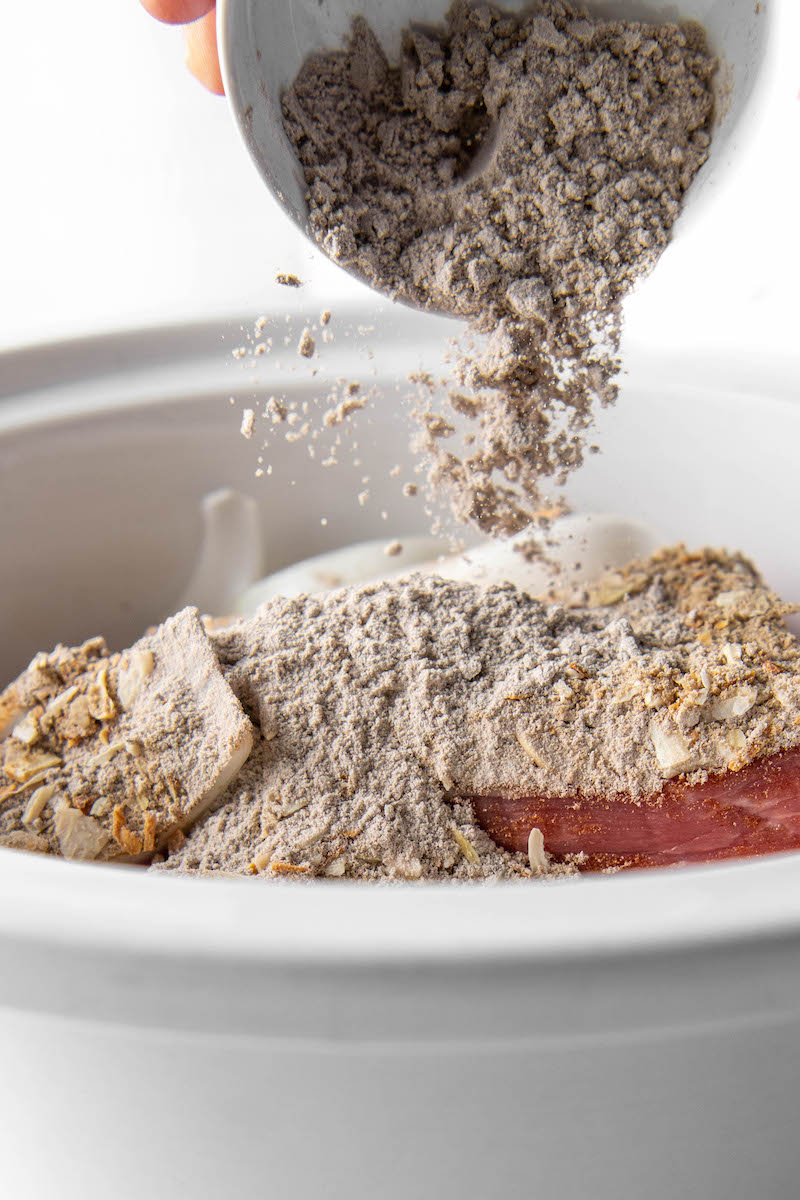 Dry brown gravy mix is sprinkled on top of raw meat in a Crockpot.
