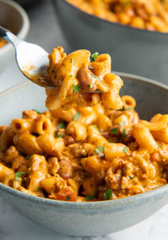 A fork is holding up a bite sized portion of chili Mac above a bowl.